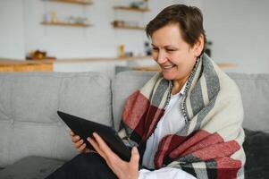 porträtt av vacker gammal kvinna som använder TabletPC och ler, sitter på soffan hemma foto