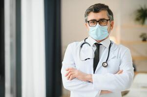 mogna gammal medicinsk sjukvård professionell läkare bär vit täcka, stetoskop, glasögon och ansikte mask. medicinsk personal hälsa vård skydd begrepp. porträtt. foto