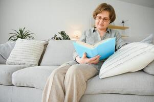 porträtt av attraktiv fokuserade glad kvinna Sammanträde på divan läsning bok tidsfördriv dagdröm på Hem hus platt inomhus. foto