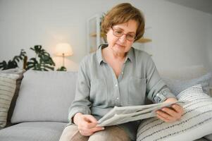 ålder och människor begrepp - Lycklig senior kvinna läsning tidning på Hem foto