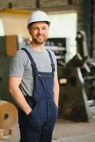 leende och Lycklig anställd. industriell arbetstagare inomhus i fabrik. ung tekniker med vit hård hatt. foto