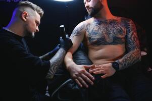 tatuering konstnär demonstrerar de bearbeta av få svart tatuering med måla. bemästra Arbetar i svart steril handskar foto