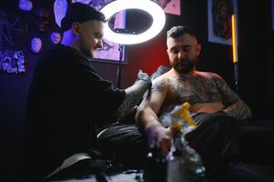 manlig tatuering konstnär innehav en tatuering pistol, som visar en bearbeta av framställning tatueringar på en manlig tatuerade modellens ärm foto