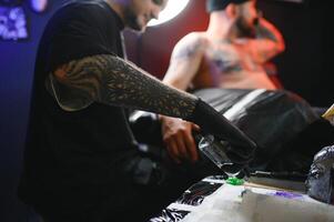 skäggig tatuering konstnär arbetssätt på hans studio tatuering ärm på de ärm av hans manlig klient. man få tatuerade förbi professionell tatuerare foto