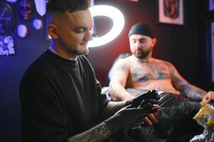 manlig tatuering konstnär innehav en tatuering pistol, som visar en bearbeta av framställning tatueringar på en manlig tatuerade modellens ärm foto