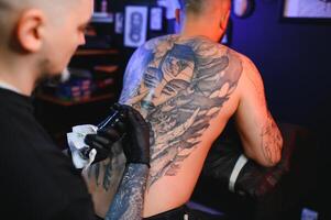 skott av en tatuering konstnär händer formning perfekt rader på man tillbaka med bläck foto