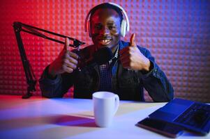afrikansk amerikan vlogger använder sig av smartphone till filma podcast i studio. bloggare med mobil telefon, mikrofon och hörlurar filmning foto