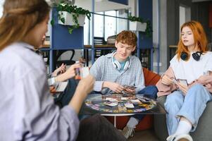 grupp av ung vänner spelar styrelse spel tillsammans medan Sammanträde runt om tabell foto