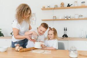 familj inlärning ny recept tillsammans. Lycklig mamma och barn blandning Ingredienser för hemlagad kaka, paj eller kaka deg i de kök. foto