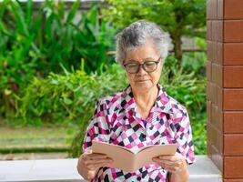 senior kvinna läsning en bok medan Sammanträde på en balkong. Plats för text. begrepp av åldrig människor och sjukvård foto