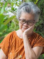 senior kvinna med kort vit hår tandvärk medan stående i en trädgård. hon är ohälsosam och har negativ tankar på liv gör henne olycklig. begrepp av åldrig människor och hälsobil foto