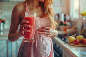 Lycklig gravid kvinna dricka grön vegetabiliska juice eller smoothie på Hem. foto