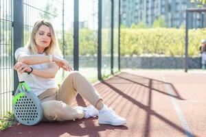 Lycklig kvinna paddla tennis spelare under öva på utomhus- domstol ser på kamera. kopia Plats. foto