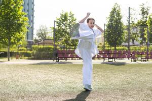 ung aktiva flicka bär i vit kimono med vit bälte utför krigisk konst sparka Kompetens. sportig karate kvinna förbättra bekämpa Metod på kinesisk bro. begrepp av sport. foto