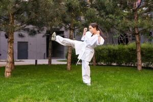 ung aktiva flicka bär i vit kimono med vit bälte utför krigisk konst sparka Kompetens. sportig karate kvinna förbättra bekämpa Metod på kinesisk bro. begrepp av sport. foto