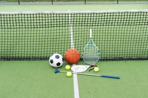 fotboll fotboll boll basketboll tennis boll och racket lagd på gräs på solnedgång foto