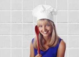 ung leende blond kock med henne färgrik sked Framställ på neutral bakgrund foto
