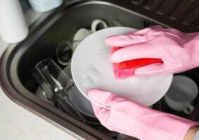 en hemmafru i rosa sudd handskar tvättar maträtter i de kök. närbild. selektiv fokus. foto