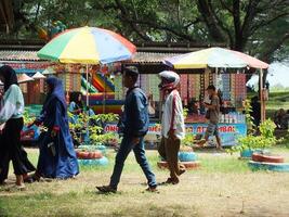 kebumen, central java, indonesien april 14, 2024 människor njut av semester under ljus dagsljus på ambal strand. sommar familj turist. en bås försäljning mat och handelsvaror foto