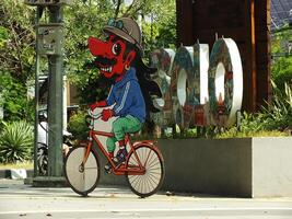 surakarta, april 11 2024, stad promenad med de ord solo- och en wayang maskot runt manahan stadion. ikoniska landmärke wayang karaktär ridning en cykel. foto