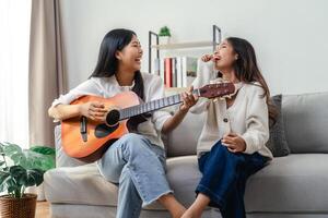 två kvinnor är Sammanträde på en soffa, ett av dem spelar en gitarr foto