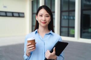 en företag kvinna bär en blå skjorta och innehav en kopp av kaffe och en läsplatta foto