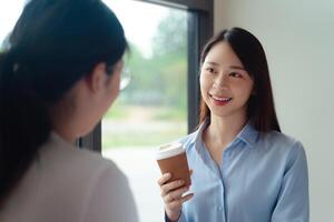 två företag kvinnor är talande och ett av dem är innehav en kaffe kopp i de kontor foto