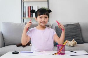 en ung flicka är Sammanträde på en tabell med en penna och en kopp av kritor foto