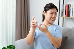 asiatisk kvinna använder sig av lansett på finger för kontroll blod socker nivå förbi glukos meter foto