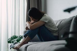 olycklig ensam deprimerad kvinna är Sammanträde på de soffa och beläggning henne ansikte med henne händer foto
