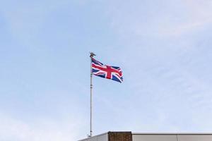 Förenade kungarikets flagga med en mås landade på stången. Englands flagga broderad på blå himmel på taket av en byggnad. foto