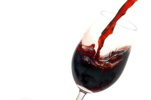 röd vin varelse eras i en glas på en vit bakgrund foto