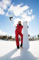 kvinna med snowboard med smartphone på en pinne för att göra selfie foto