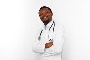 leende svart skäggig läkare man korsade vapen i vit täcka med stetoskop, vit bakgrund foto
