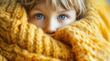 barn kikar från gul filt. ett förtjusande ung barn kikar ut med stor blå ögon från en mysigt gul stickat filt. . foto