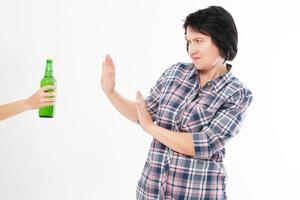 medelålders kvinna avvisar en hand med en isolerad ölflaska - kvinnligt alkoholberoende koncept foto