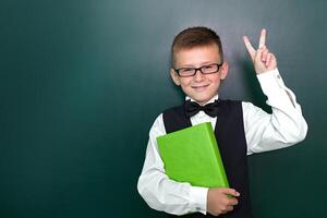 Lycklig söt duktig pojke med en rosett slips och i glasögon med bok i hans hand. först tid till skola. tillbaka till skola. foto