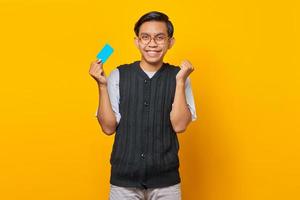 upphetsad ung asiatisk man som håller kreditkort isolerad på gul bakgrund foto