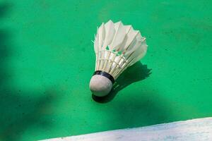 de badminton fjäderboll och dess skugga är på de grön domstol golv. foto