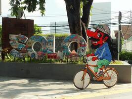 surakarta, april 11 2024, stad promenad med de ord solo- och en wayang maskot runt manahan stadion. ikoniska landmärke wayang karaktär ridning en cykel. foto