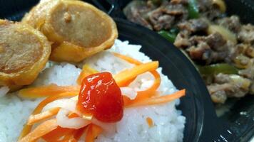 japansk ris maträtt som innehåller ris, nötkött teriyaki, sallad och klä på sig, och friterad snacks foto