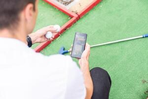 Rör skärm i hand, läsplatta på golf klubb. smartphone med en sporter vadhållning Ansökan foto