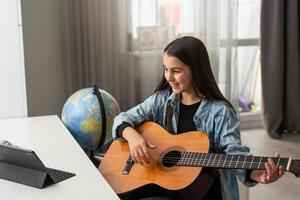 tonåring flicka inlärning till spela gitarr på Hem använder sig av uppkopplad lektioner. hobby avlägsen musikalisk utbildning akustisk gitarr. kopia Plats foto