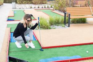 kvinna spelar mini golf och påfrestande sätta boll in i hål. sommar fritid aktivitet foto