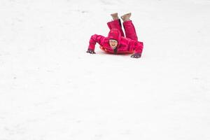 barndom, släde och säsong begrepp - Lycklig liten flicka glidning ner på kälke utomhus i vinter- foto