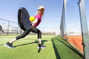 sportigt ung flicka med racketen spelar padel i de öppen domstol utomhus foto