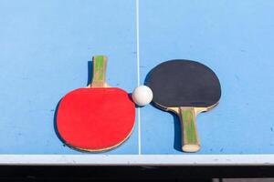 röd och svart tabell tennis paddlar och boll på de blå tabell tennis tabell med netto. ping pong begrepp med kopia Plats foto