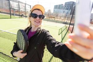 Lycklig kvinna paddla tennis spelare under öva på utomhus- domstol ser på kamera. kopia Plats. foto