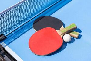 två tabell tennis eller ping pong racketar och boll på blå tabell med netto foto