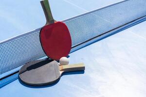 två tabell tennis eller ping pong racketar och boll på blå tabell med netto foto